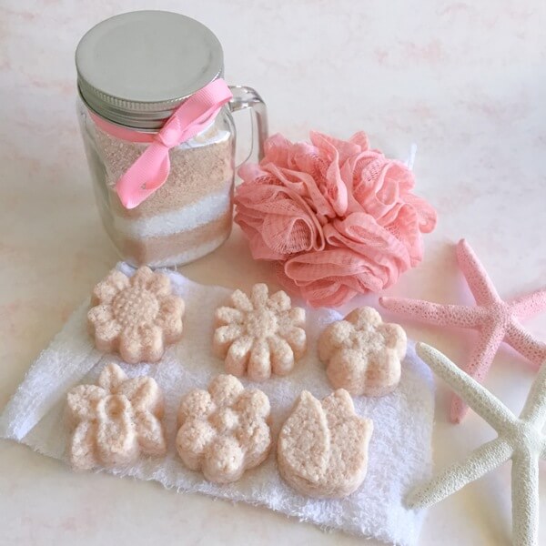 a jar of bath salts with a pink loofah sponge and six pink bath salt cakes