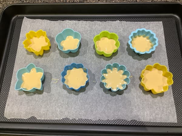 eight 5cm flower silicone moulds filled with caramilk chocolate laid out on a tray