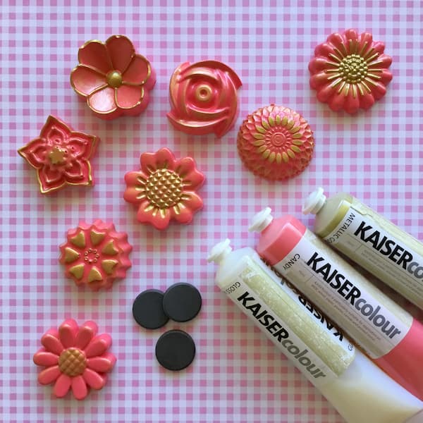 plaster flowers sitting next to pink and gold paint tubes and three round magnets