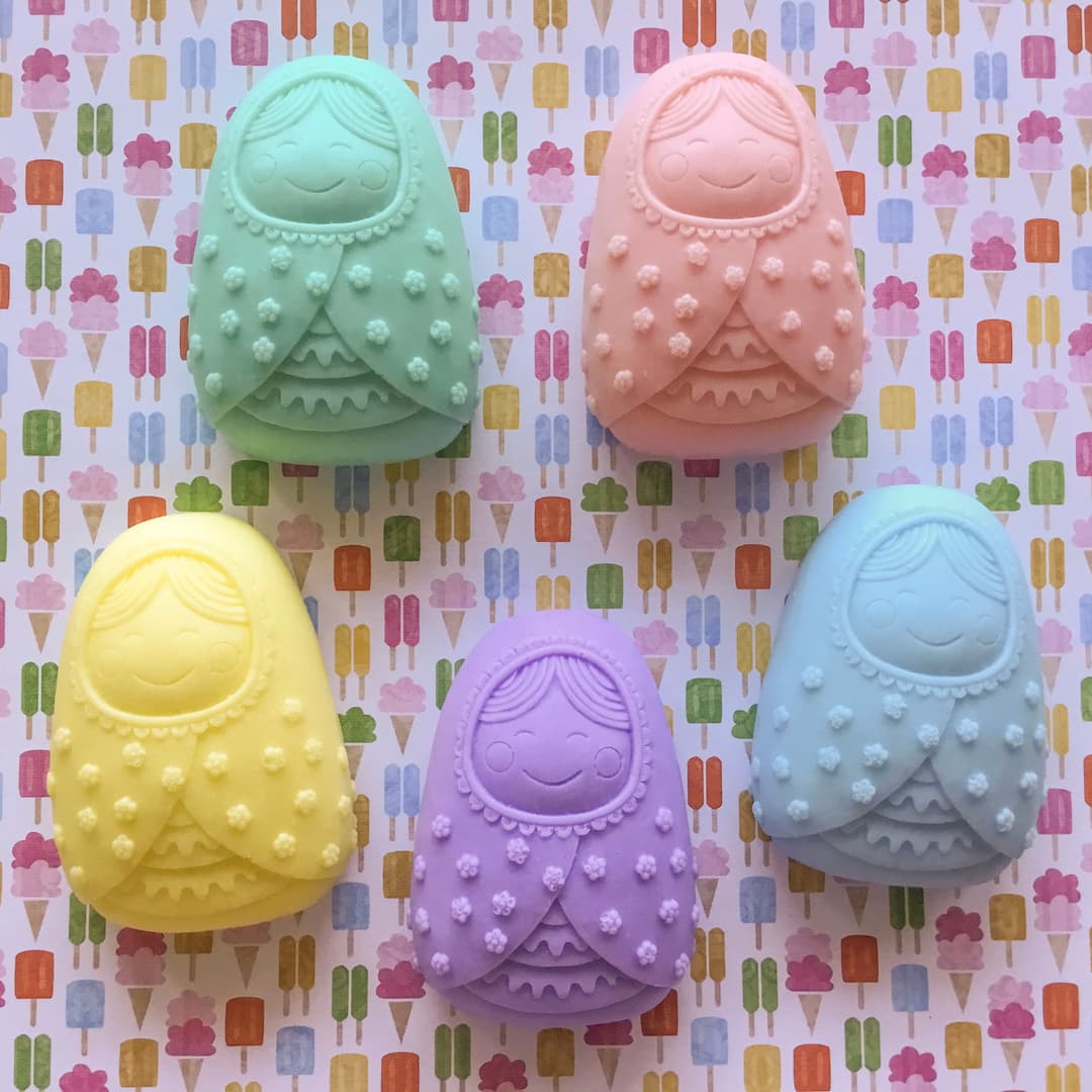 five soap bars in the shape of baby dolls laid out clockwise pink, blue, purple, yellow, green