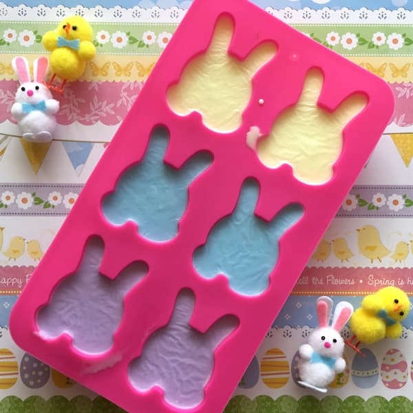 dark pink silicone mould of bunny rabbits filled with yellow, blue and purple soap