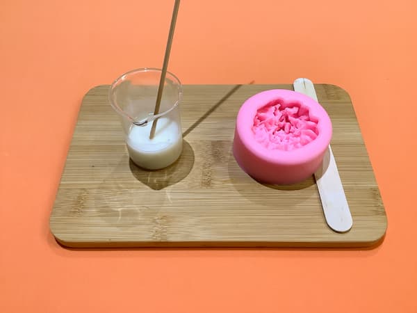 a beaker of melted soap base sitting next to a carnation soap mould