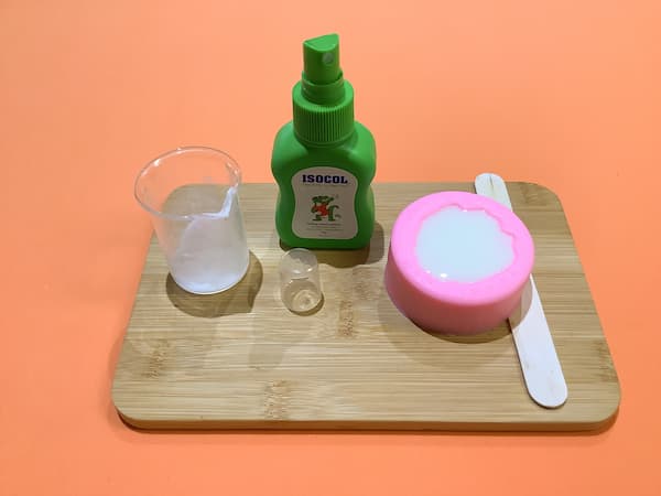 a carnation soap mould filled with freshly-poured soap sitting next to a bottle of rubbing alcohol and an empty glass beaker