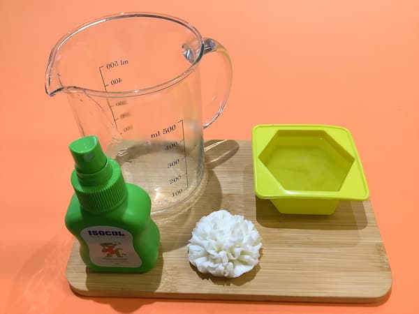 a silicone mould in the shape of a hexagon filled with recently-poured clear soap base sitting next to an empty glass jug and a bottle of rubbing alcohol