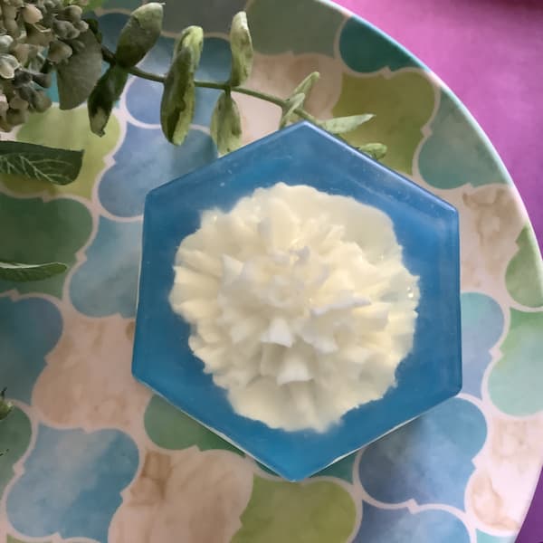 white soap carnation embedded in a clear hexagonal soap bar with a dark blue background