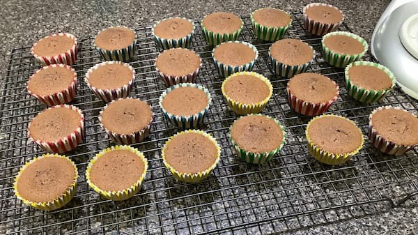 24 freshly baked chocolate cupcakes on a cooling rack